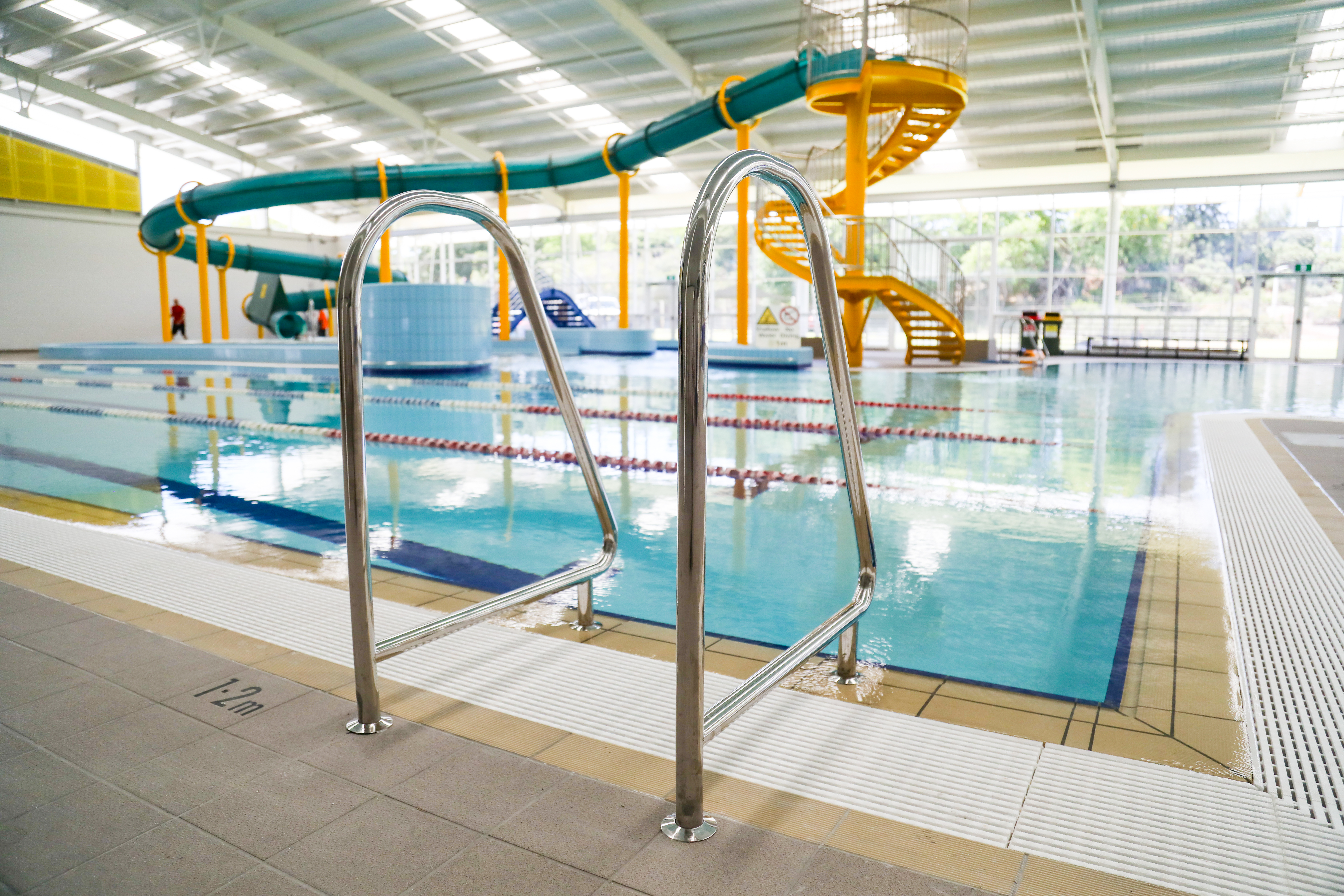 A close up photo of a pool ladder, with the indoor waterslide in the background