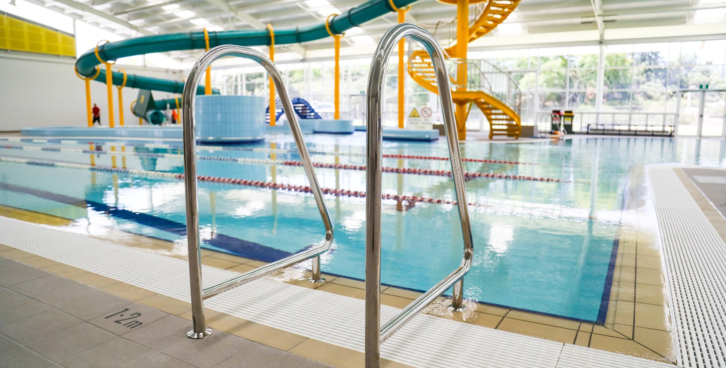 A close up photo of a pool ladder, with the indoor waterslide in the background