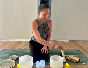 Sound Healing instructor kneeling on a mat playing bowls