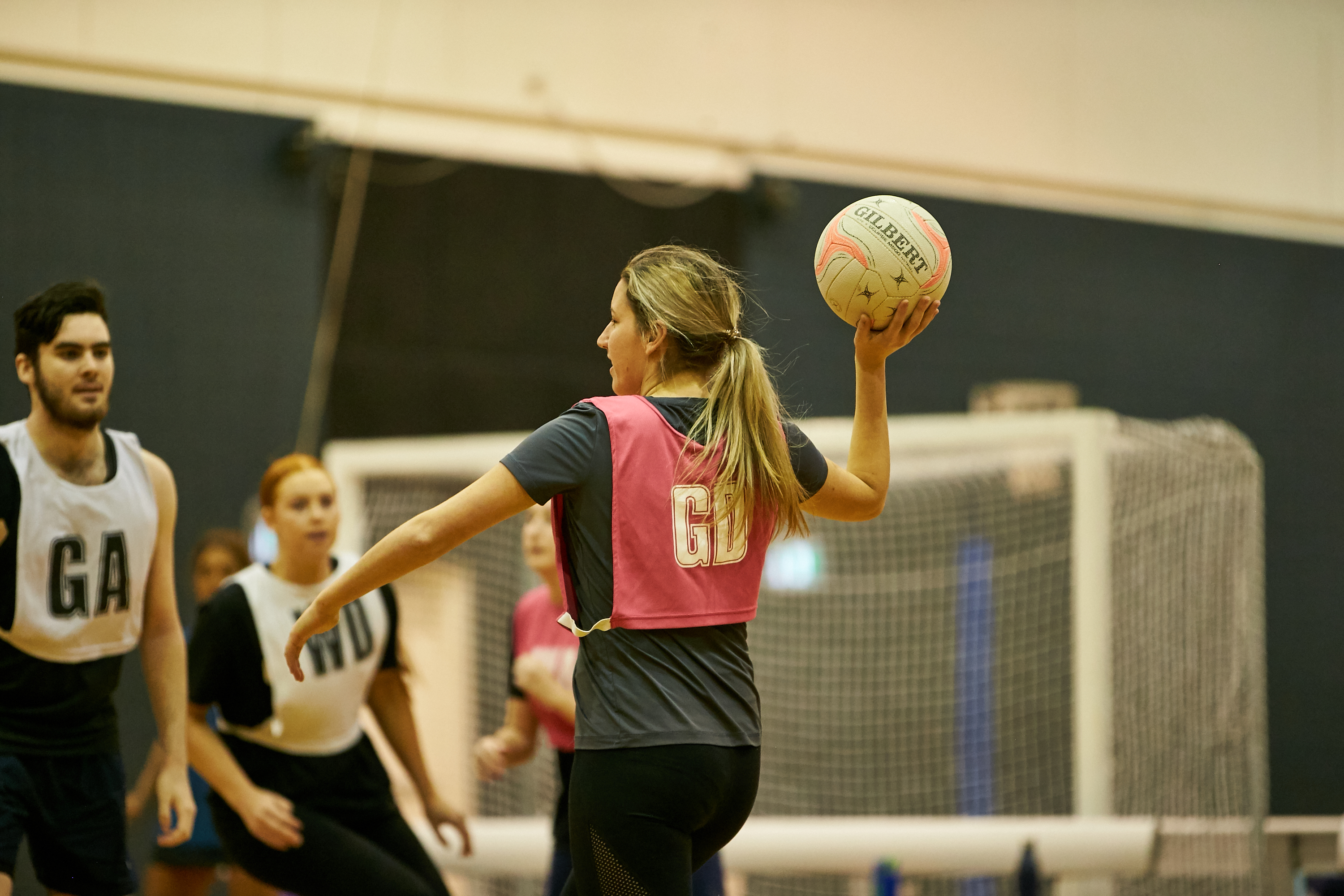 A photo of a female netball player holding the ball in a throwing motion with two other players in the background