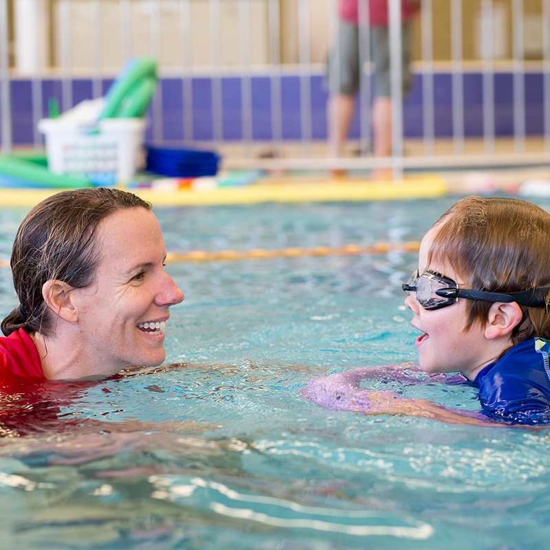 Swim instructor in the water teaching a young boy to swim