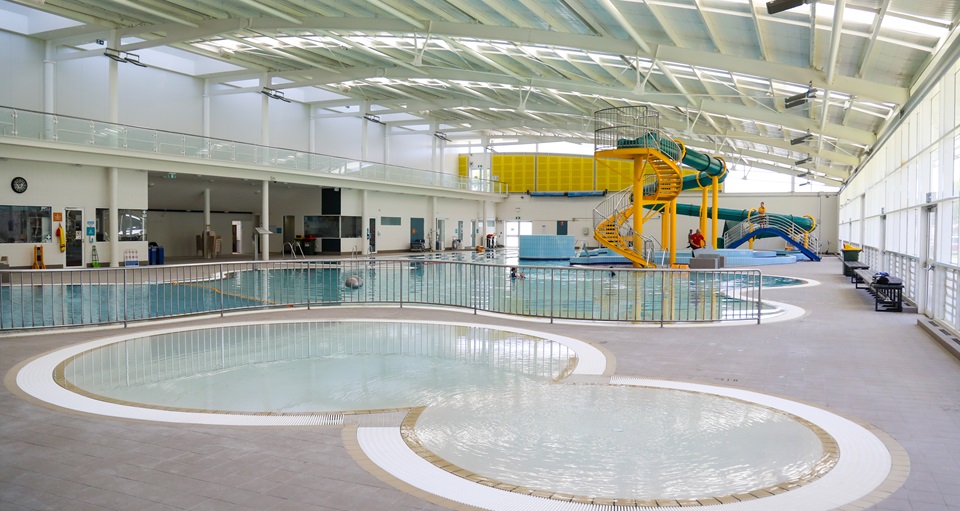 A photo of a small kids pool with the main indoor pool in the background