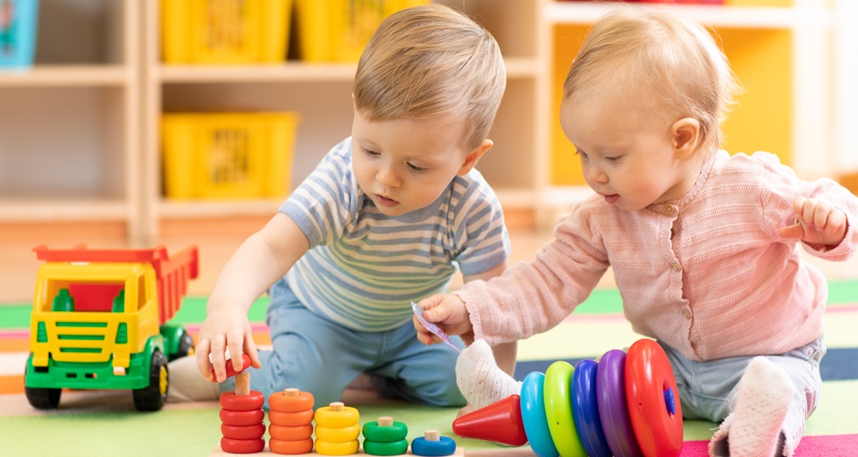 A photo of two babies playing with blocks and toys